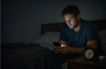 Person sitting on a bed at night while looking at a phone