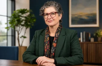 Elizabeth Fogle in a professional portrait wearing glasses and formal clothing in a modern office setting.