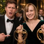 Emma Nesper smiling at an award event while holding two gold trophies beside a man in formal wear.